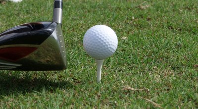 A golf ball sits on a tee in the grass with a driver lining up a shot to the left