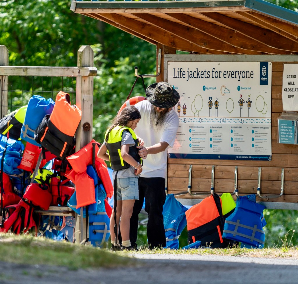 An adult helps a child into a life jacket in front of a free life jacket station at a Metro Park. That is one of the top water safety tips.